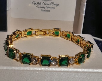 May include: A gold bracelet with emerald green and clear square-shaped stones. The bracelet is in a white box with the text "White Swan Design Wedding Accessories Handmade".