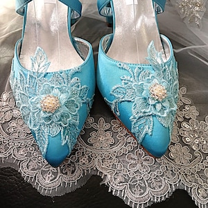 Pode incluir: Um par de sapatos de noiva de cetim azul-turquesa com bordados florais e detalhes de p&eacute;rolas. Os saltos abertos apresentam detalhes delicados em renda e tiras cruzadas. Sapatos para uma ocasi&atilde;o especial.