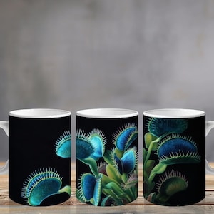 May include: A white ceramic mug featuring a wrap-around graphic of multiple Venus flytrap plants against a solid black background. The plants have vibrant blue-tinted traps with sharp, spiky edges and green stems, displayed in a repeating pattern.