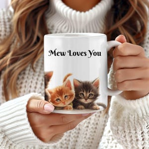 May include: White ceramic mug with a black and white image of three kittens. The mug has the text "Mew Loves You" printed on the front.