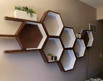 May include: A wall-mounted hexagonal shelf unit made of dark wood with white accents. The shelves are arranged in a honeycomb pattern and have a modern, minimalist design.