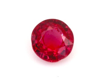 Könnte beinhalten: Ein facettierter, rund geschliffener Rubin-Edelstein. Der Edelstein hat eine tiefe, leuchtende rote Farbe mit sichtbaren Innenfacetten, die das Licht einfangen und reflektieren. Der Rubin liegt vor einem schlichten weißen Hintergrund.