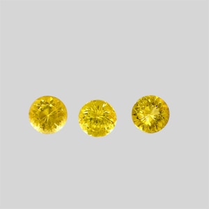 May include: Three round, yellow gemstones with a faceted cut.