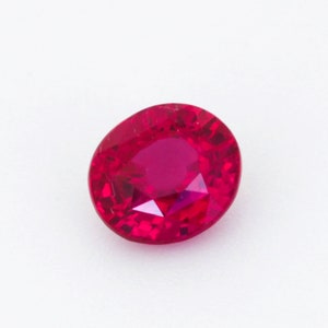 Peut inclure: Une pierre précieuse ovale de couleur rouge vif avec une taille facetée. La pierre précieuse est placée sur un fond blanc.