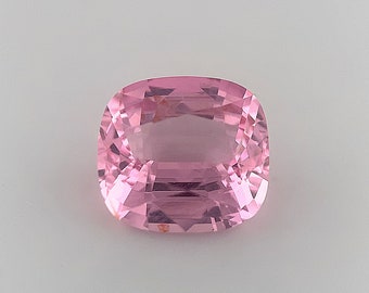 May include: A light pink gemstone with a cushion cut. The gemstone is faceted and has a translucent appearance.
