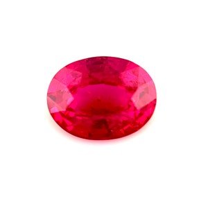 May include: A vibrant, oval-shaped ruby gemstone. The gem is a deep, saturated red color with a polished surface, set against a clean white background. The gemstone's facets catch the light, creating a sparkling effect.