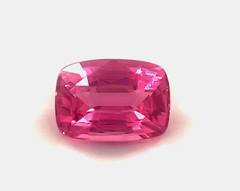 May include: A vibrant pink gemstone with a cushion cut. The gemstone is faceted and has a high polish.