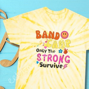 Può includere: Maglietta gialla tie-dye con il testo "Bando Camp Only The Strong Survive" in lettere e grafiche colorate.