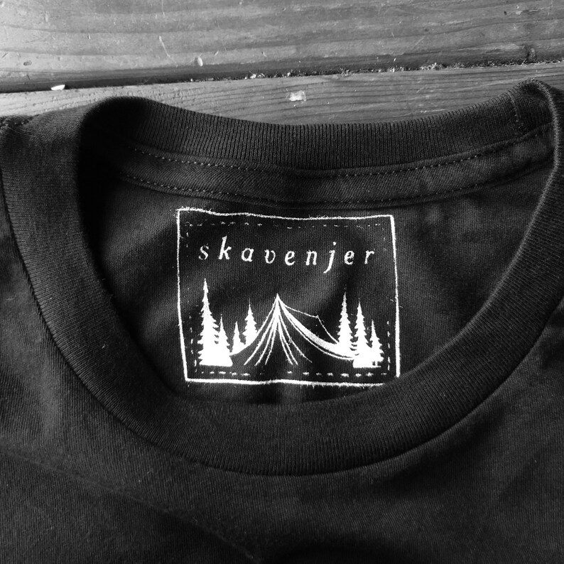 May include: Black crew neck t-shirt with a white rectangular graphic. The graphic features the word "skavenjer" above a tent and pine tree design. The shirt is made of a soft, comfortable material.