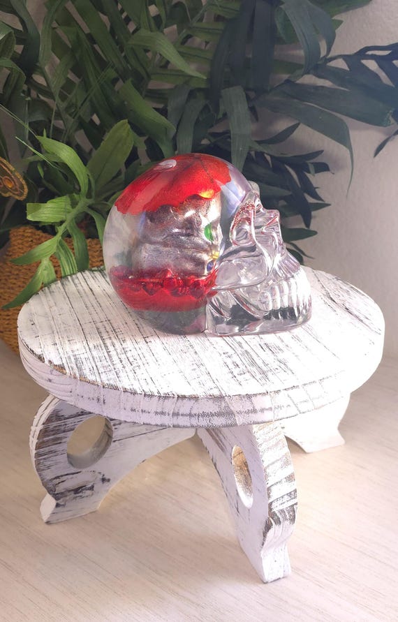 A clear resin skull with a miniature metallic red apple-core skeleton scene frozen inside — it's a macabre diorama you can hold in your hand.