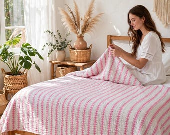 May include: A white quilt featuring vertical stripes of pink triangular patterns. The quilt has a visible stitched texture throughout the fabric, creating a quilted appearance. The design consists of repeating pink geometric shapes arranged in lines.
