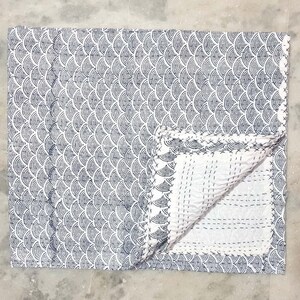 Puede incluir: Una colcha de algodón blanco con un patrón geométrico azul y blanco. La colcha está doblada por la mitad y el patrón es visible en ambos lados.