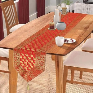 May include: Red and gold table runner with an elephant pattern. The runner is on a wooden table with two chairs.