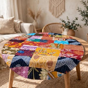 May include: A round patchwork tablecloth featuring a variety of colorful fabric squares with diverse patterns, including floral, geometric, and abstract designs in shades of red, yellow, blue, and purple, finished with visible white stitching.