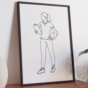 Könnte beinhalten: Ein gerahmter Kunstdruck mit einer schwarzen einzeiligen Zeichnung einer stehenden Person, die ein Klemmbrett in der einen Hand und eine zusammengerollte Matte unter dem anderen Arm hält. Das Bild ist in einem dünnen schwarzen Rahmen eingefasst.
