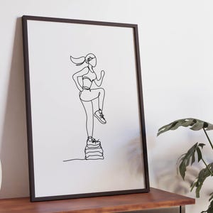 Op de afbeelding: Ingelijste kunstdruk met een minimalistische lijntekening van een persoon die aan het sporten is. Het kunstwerk toont een figuur in sportkleding, in beweging, die op een stapel objecten stapt. De tekening staat tegen een witte achtergrond.
