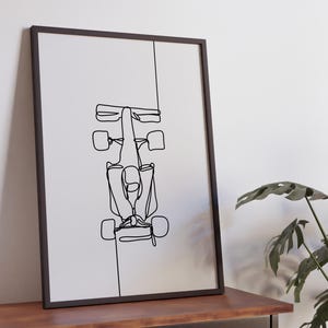May include: Black and white line art print of a race car driver in a Formula One car. The print is framed in a black frame and is hanging on a white wall.