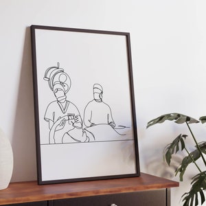 Puede incluir: Un dibujo en blanco y negro de tres profesionales médicos realizando una cirugía. El dibujo está enmarcado en un marco negro y está colgado en una pared blanca.