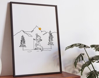 May include: A black framed print of a line drawing of a person hiking with a dog in the mountains. The sun is setting behind the mountains.
