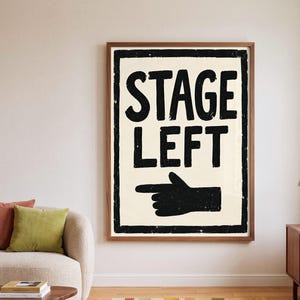 May include: A rectangular wall art print featuring a cream-colored background with a thick black border. The text STAGE LEFT is printed in bold black capital letters above a black hand icon pointing to the left with a distressed texture.