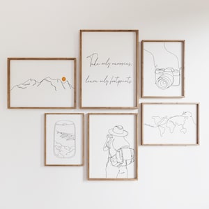 Op de afbeelding: Een set van zes minimalistische lijnkunstprints in zwart-wit met houten frames. De prints tonen een bergketen, een wereldkaart, een camera, een vliegtuigraam, een vrouw met een rugzak en een citaat dat luidt: "Neem alleen herinneringen mee, laat alleen voetafdrukken achter".