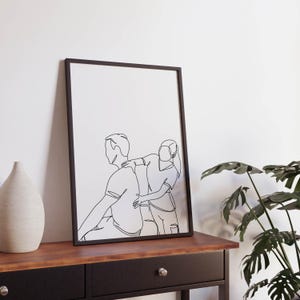 May include: A black framed print with a line drawing of a couple. The woman is standing behind the man, with her arm around his shoulder. The drawing is in a minimalist style.
