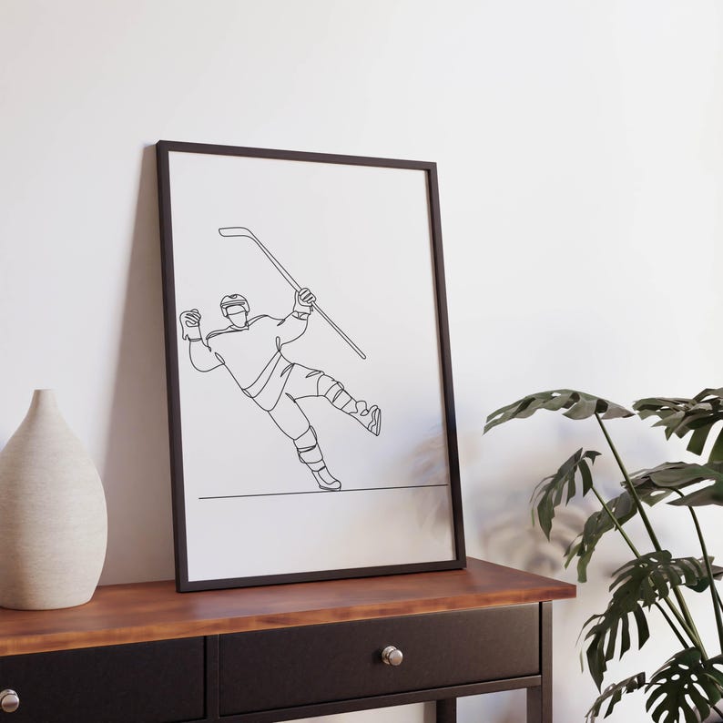 May include: A black and white line drawing of a hockey player skating and holding a hockey stick. The drawing is framed in a black frame and is hanging on a wall.