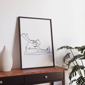 May include: Black and white line art print of a person stretching in a yoga pose. The print is framed in a black frame and is hanging on a white wall.