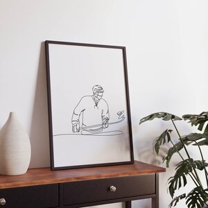 May include: Black and white line art print of a hockey player in a helmet, holding a hockey stick and skating on ice. The print is framed in a black frame and hanging on a white wall.