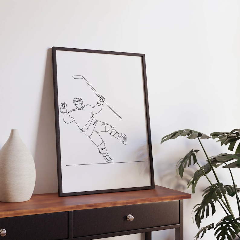 May include: Black and white line art print of a hockey player in a framed poster. The player is in mid-air, holding a hockey stick and about to shoot the puck.