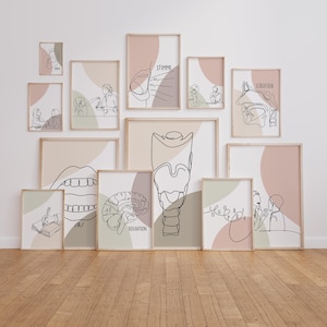 May include: A set of framed art prints featuring line drawings of human anatomy and figures. The prints use neutral colours, including beige, pink, and green, with text in German. The art is displayed on a white wall above a wooden floor.