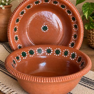 May include: Two round terracotta bowls with a smooth, glazed finish. Each bowl features a decorative rim with vertical ridges and a hand-painted pattern of dark green dots surrounded by small white dots along the interior edge and center.