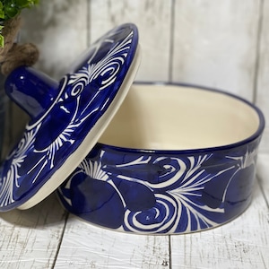 May include: A blue and white ceramic serving bowl with a lid. The bowl has a floral design with white swirls on a blue background. The lid has a knob on top.