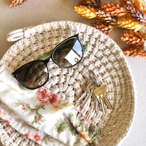 May include: A white crocheted tray with a floral fabric, sunglasses, and keys. The tray is on a beige surface.