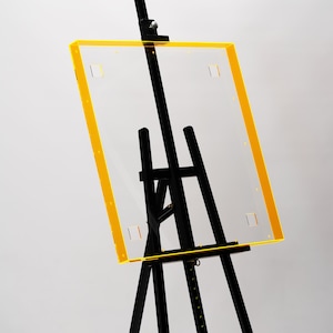 Peut inclure: Un chevalet noir avec un panneau en acrylique transparent encadré de jaune. Le panneau est fixé au chevalet à l'aide de vis.