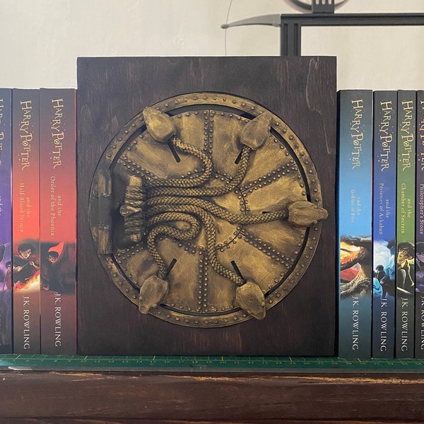 May include: A set of seven Harry Potter books, with the first book, "Harry Potter and the Philosopher's Stone", on the right and the last book, "Harry Potter and the Deathly Hallows", on the left. The books are arranged on a wooden shelf with a decorative bookend featuring a golden snake design.
