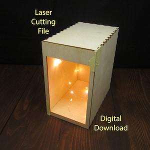 Könnte beinhalten: Eine Holzkiste mit einem Licht im Inneren. Die Kiste ist aus Sperrholz und hat ein schlichtes Design. Das Licht ist eine Lichterkette mit weißen LED-Leuchten. Die Kiste ist mit "Laser Cutting File" und "Digital Download" beschriftet.