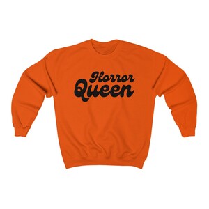 Może przedstawiać: Pomarańczowa bluza z czarnym napisem "Horror Queen" w retro czcionce.