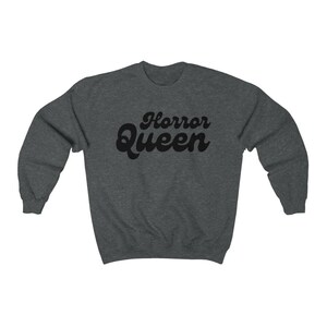 Może przedstawiać: Ciemnoszara bluza z napisem "Horror Queen" w czarnym, retro kroju czcionki. Bluza ma okrągły dekolt i długie rękawy. Tekst jest wyśrodkowany na klatce piersiowej.