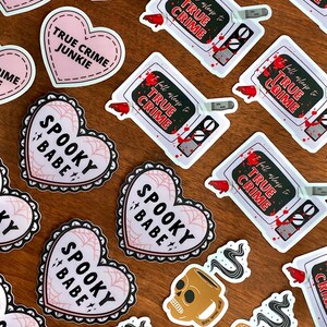 May include: Assortment of stickers featuring various designs, including hearts with the text "Spooky Babe" and "True Crime Junkie", and a television with the text "Fall Asleep to True Crime".