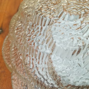 May include: Close-up of a clear glass lampshade with a textured, rippled surface. The lampshade has a scalloped edge and is made of thick glass.