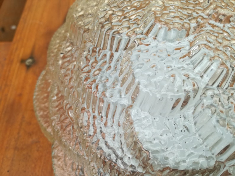 May include: Close-up of a clear glass lampshade with a textured, rippled surface. The lampshade has a scalloped edge and is made of thick glass.