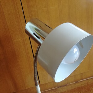 May include: A white and chrome desk lamp with a flexible arm and a white shade. The lamp is turned on and the light bulb is visible.