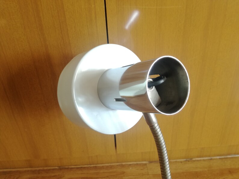 May include: A white and chrome adjustable lamp with a flexible arm. The lamp has a standard light bulb socket.