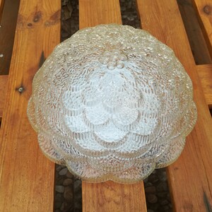 May include: A clear glass ceiling light fixture with a textured, flower-like design. The light fixture has a rounded shape and a scalloped edge.