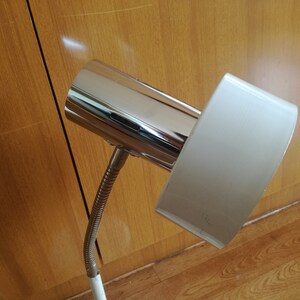 May include: A chrome and white desk lamp with a flexible arm. The lamp has a cylindrical chrome base and a rectangular white shade.