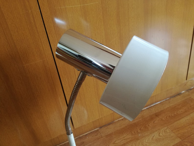 May include: A chrome and white desk lamp with a flexible arm. The lamp has a cylindrical chrome base and a rectangular white shade.