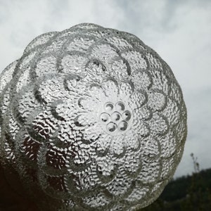 May include: A clear glass bowl with a textured, floral design. The bowl has a raised center with a circular pattern of small, raised dots.