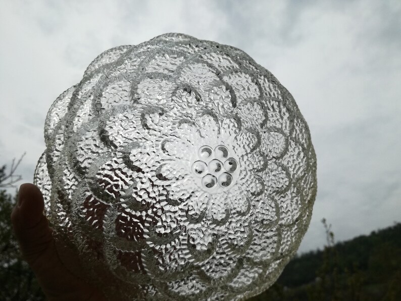 May include: A clear glass bowl with a textured, floral design. The bowl has a raised center with a circular pattern of small, raised dots.