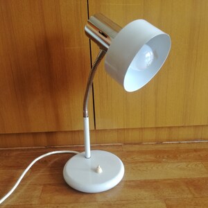 May include: A white desk lamp with a flexible arm and a white shade. The lamp has a chrome base and a chrome switch.